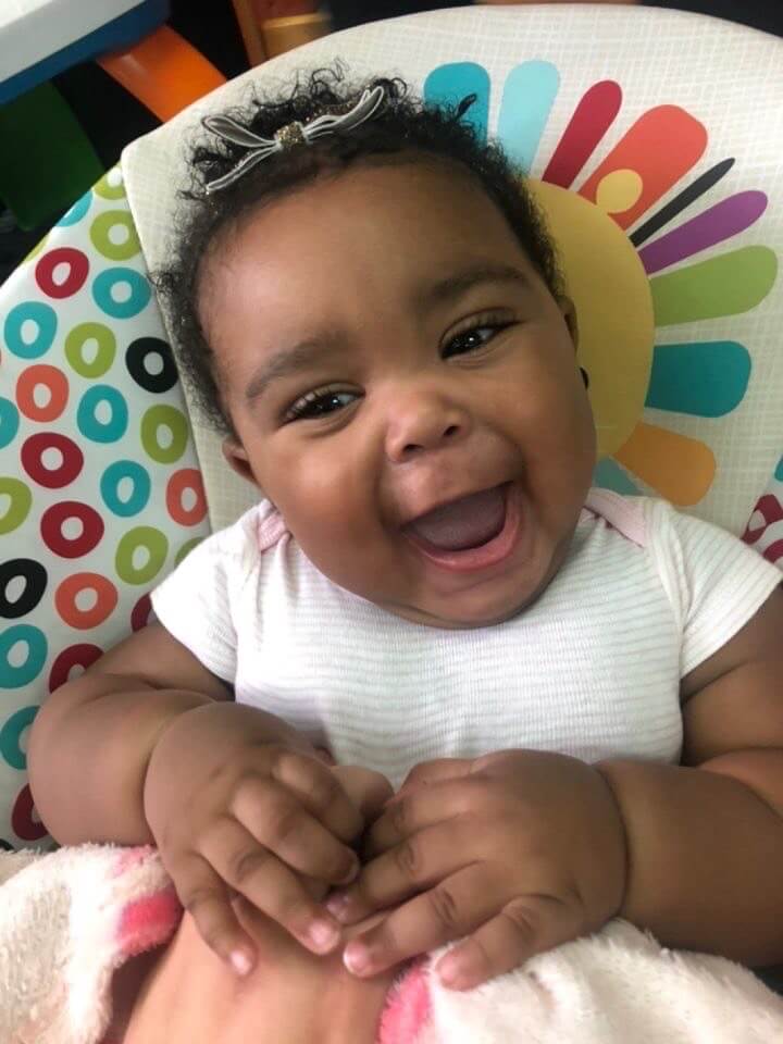 Smiling baby in colorful high chair.