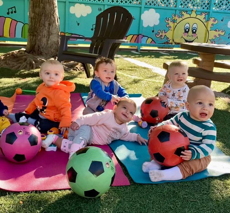 Babies playing with colorful soccer balls outdoors.
