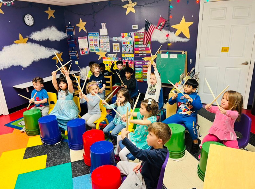 Children drumming with sticks in colorful classroom.