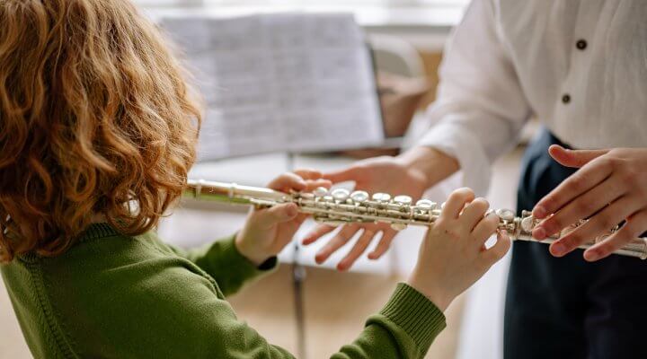 child playing flute with teacher reaching for some helping hands