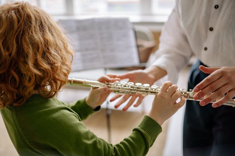 child playing flute with teacher reaching for some helping hands. Engaging children with age-appropriate music activities can stimulate brain development, promote self-expression, and help build friendships based on shared interests. Drool of Rock in Cockeysville, Maryland and Owings Mills, Maryland has established a full curriculum to deliver on this learning philosophy.