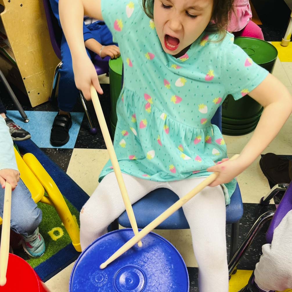 Child enthusiastically drumming on plastic bucket.