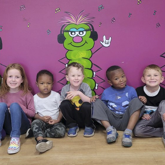 Five children sitting in front of a wall with a painted caterpillar on it. Discover the exceptional childcare and education experience offered at our preschool education center in Owings Mills, Maryland. Enroll today!