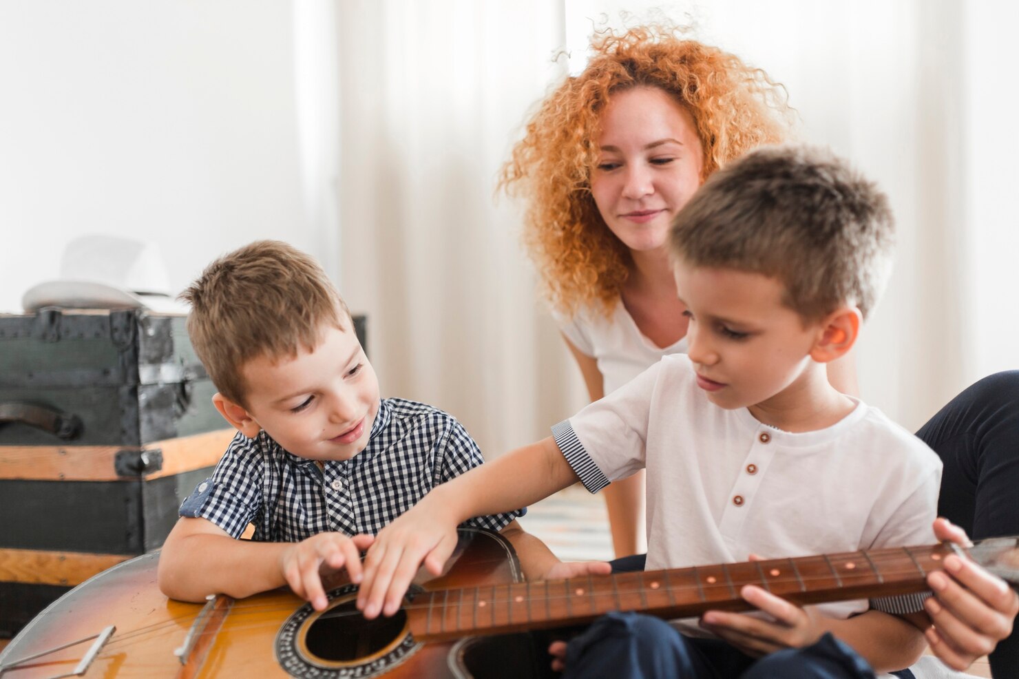 Children learning guitar with adult supervision.