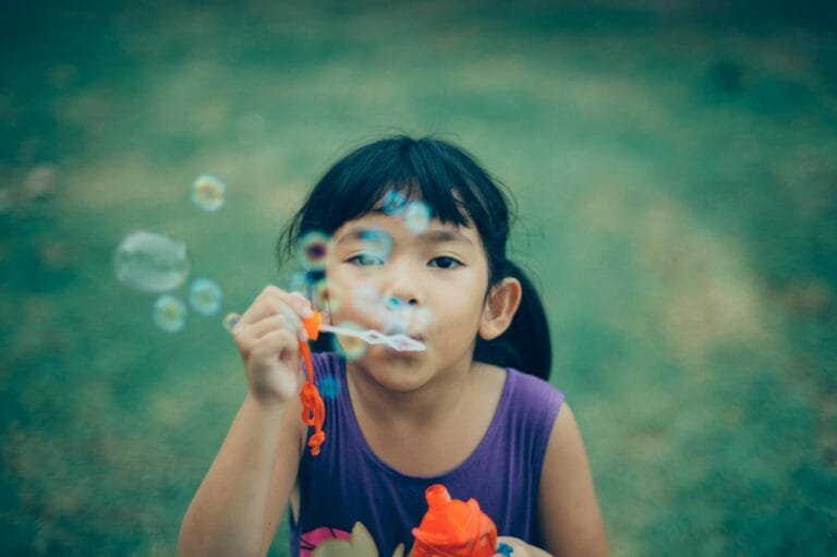 Adorable young girl enjoying summer outdoors while blowing bubbles, capturing pure childhood joy.